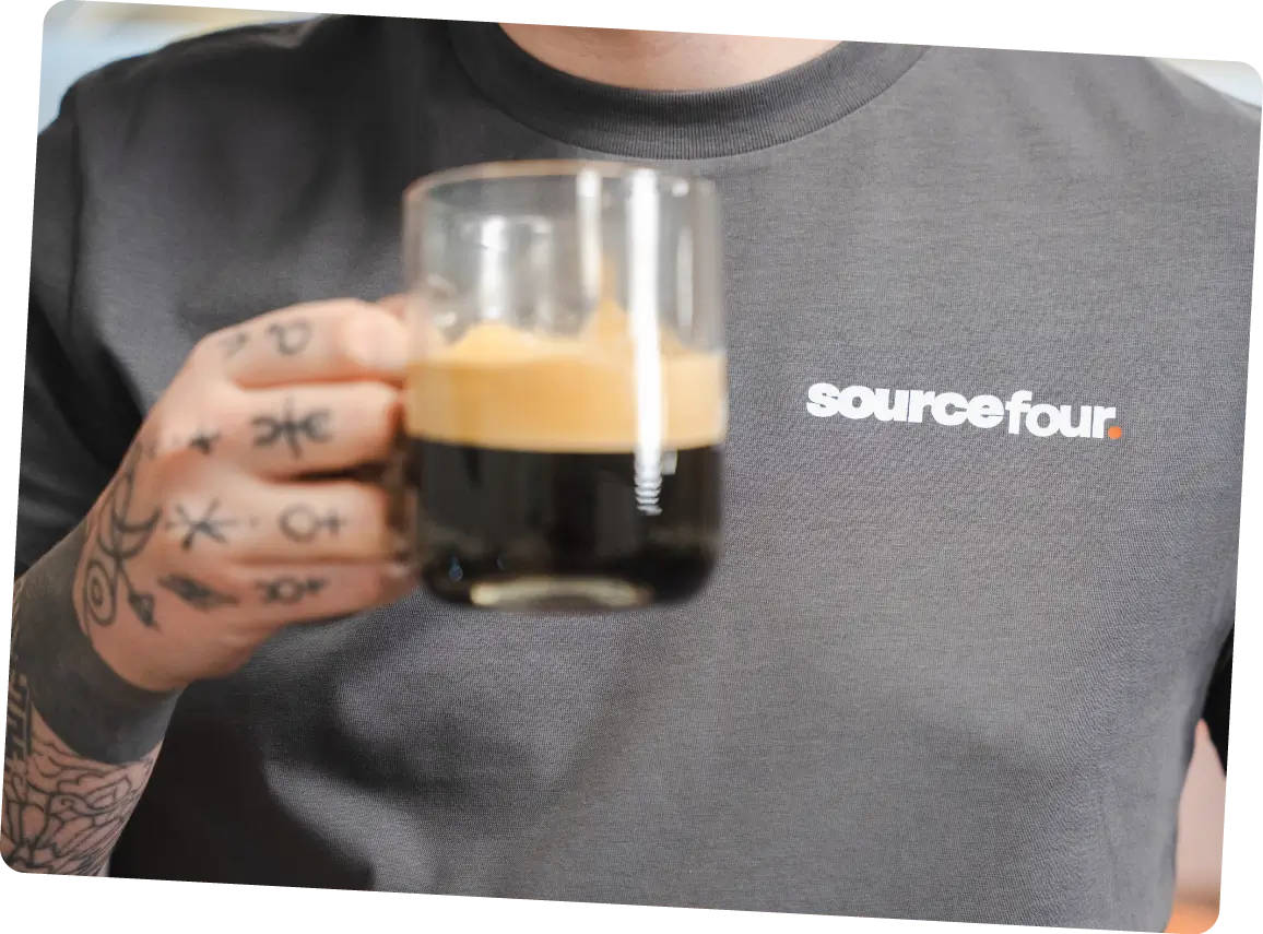A man holding a black coffee wearing a grey Sourcefour t shirt