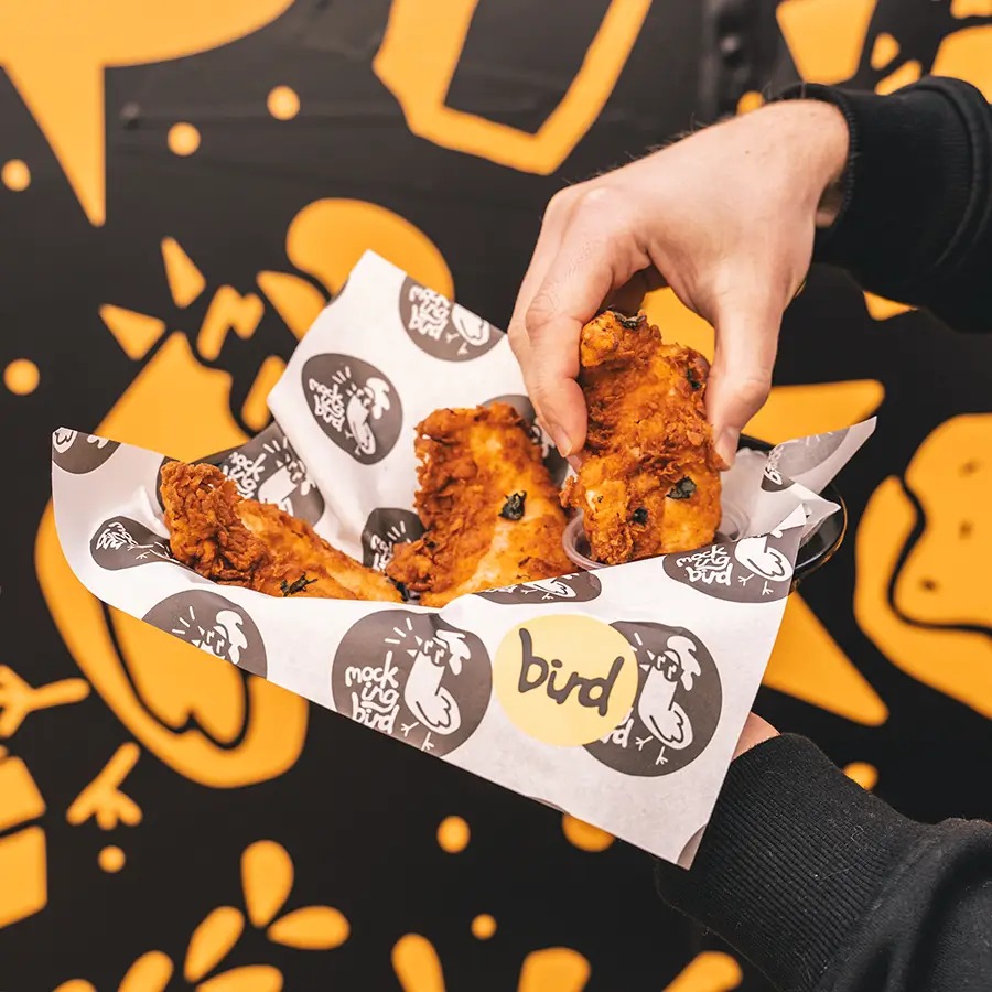 Someone grabbing Mockingbird chicken wraps out of a Mockingbird themed basket